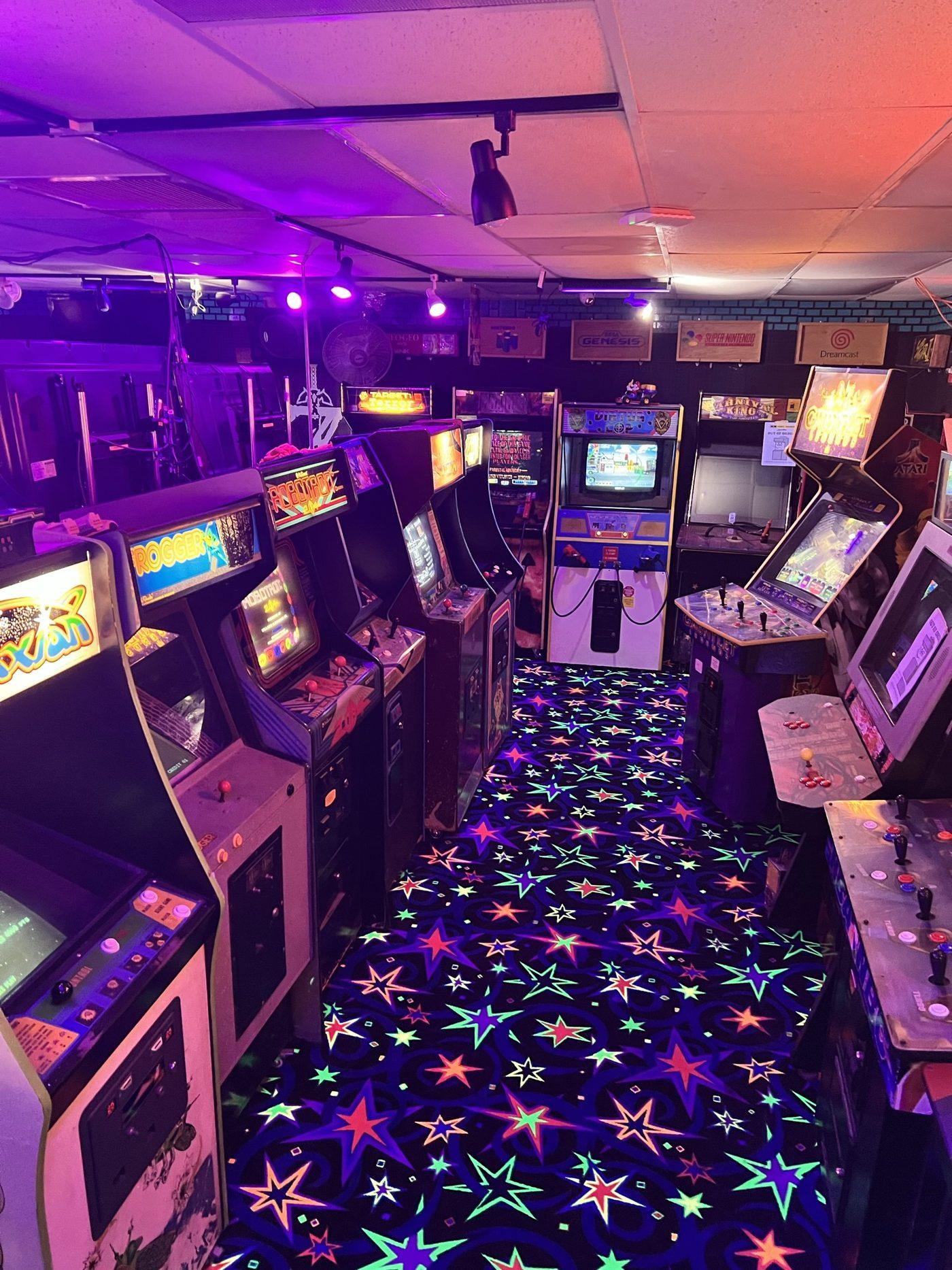The arcade room lit purple with cabinets on both sides